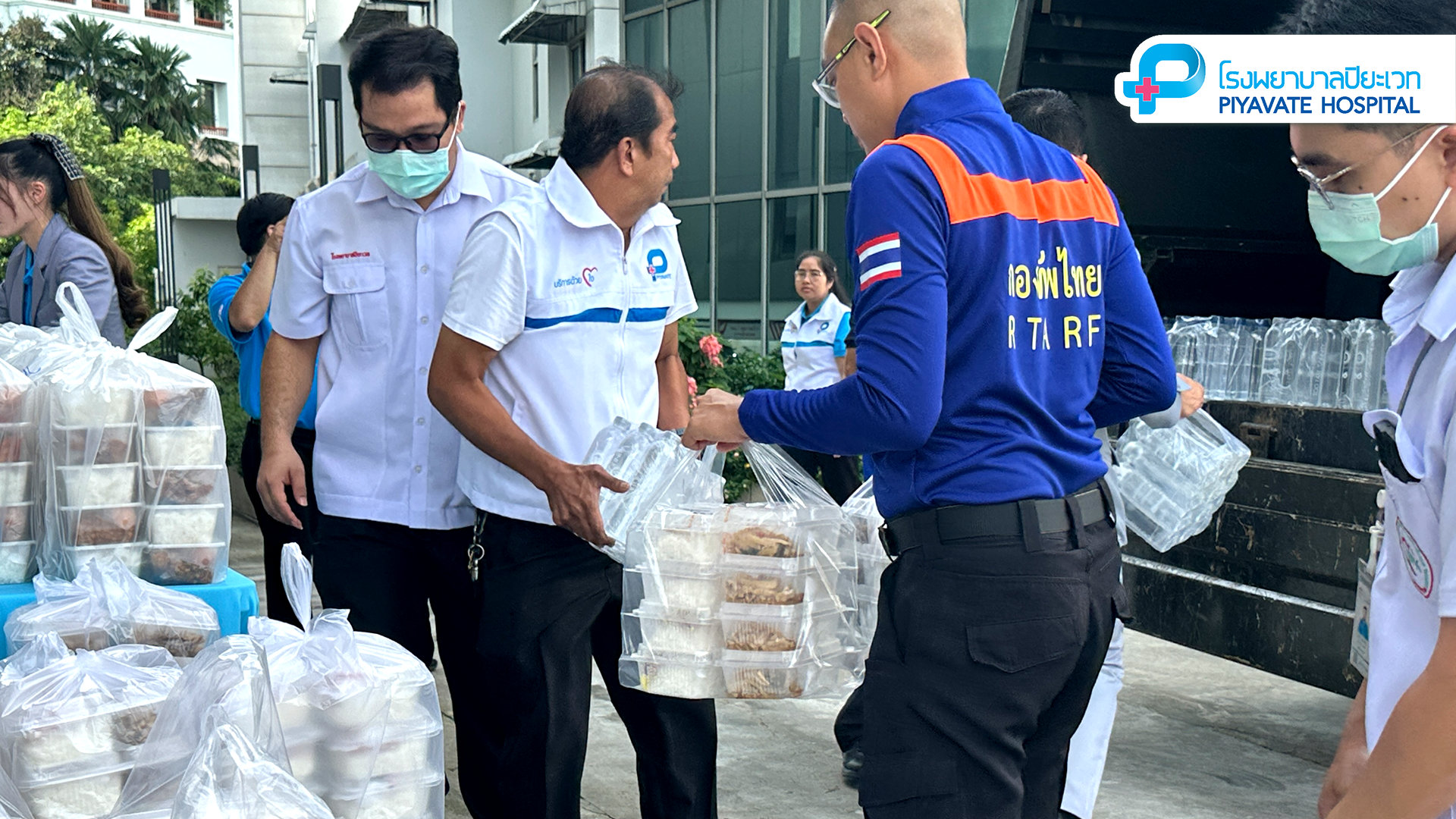 เจ้าหน้าที่กำลังถืออาหารกล่องและน้ำดื่มบรรจุขวดเพื่อโหลดขึ้นรถส่งของ