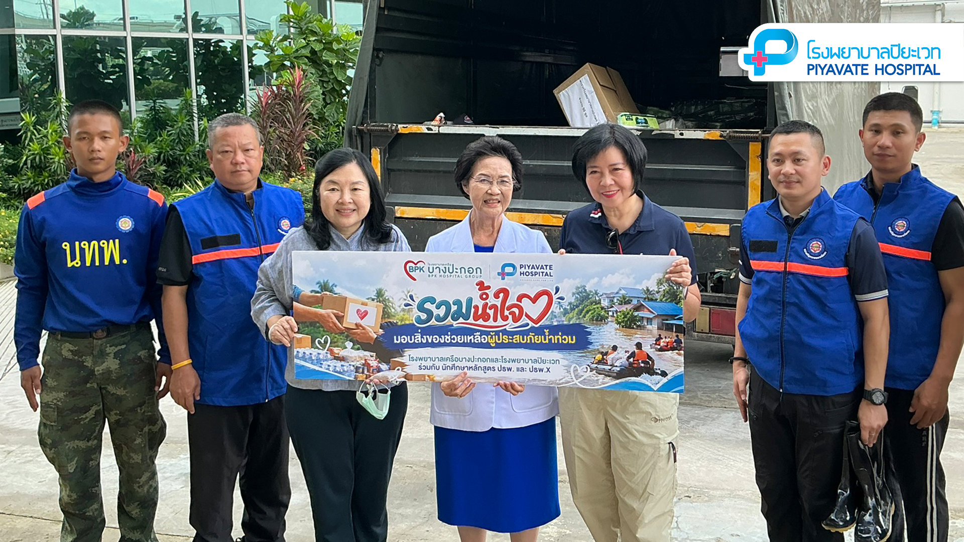 พญ.เจรียง จันทรกมล ถือป้ายช่วยเหลือรวมน้ำใจร่วมกับอาสาสมัครหน้าตัวรถบรรทุก